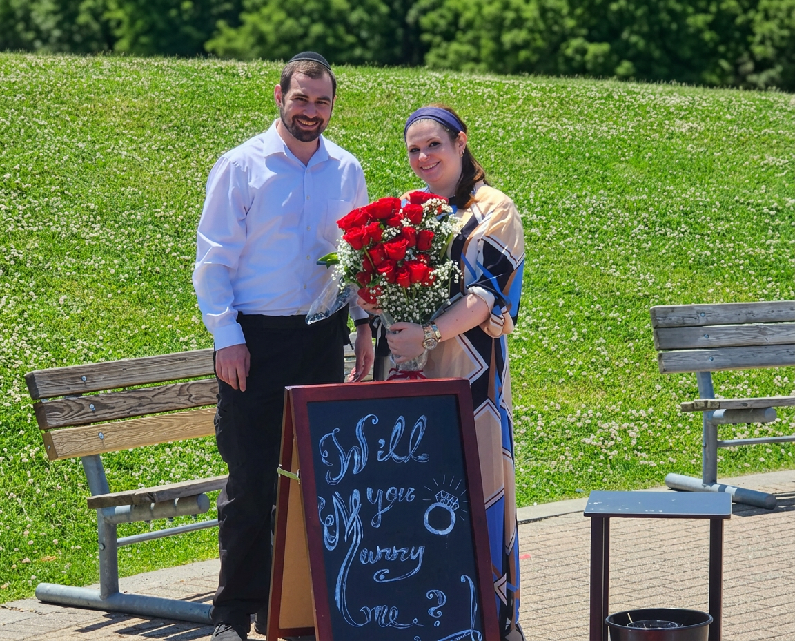Nachum and Bracha after the proposal with red roses and a Will you marry me sign